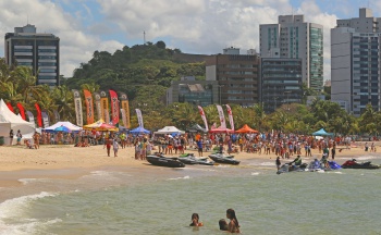 Curva da Jurema vista do mar, com banhistas, velas e pranchas da competição Aloha Spirit e o Moorro do Cruzeiro ao fundo